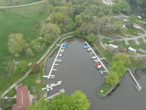 Aerial view of a marina with boats docked, surrounded by greenery and a camping area.