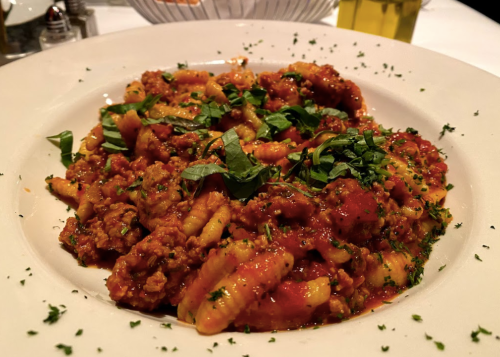 A plate of pasta with a rich meat sauce, topped with fresh basil and herbs, served on a white dish.