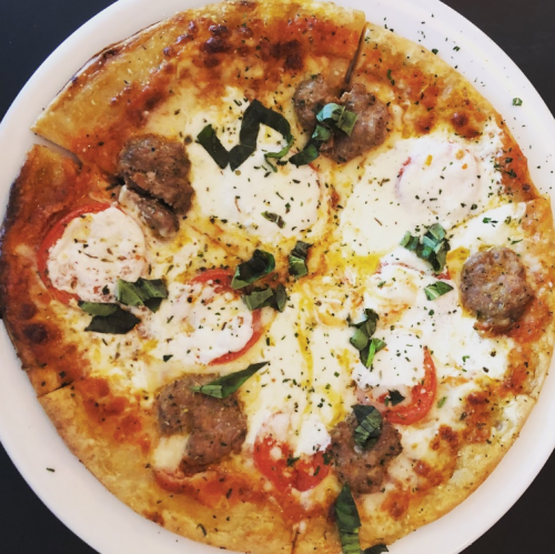 A delicious pizza topped with mozzarella, sausage, tomatoes, and fresh basil on a golden crust.