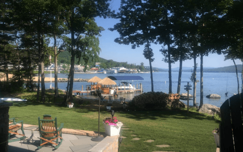 Scenic lakeside view with boats, a dock, and lush greenery under a clear blue sky.