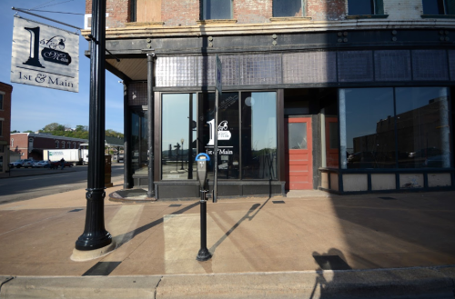 A street view of a corner building at 1st and Main, featuring large windows and a sign.