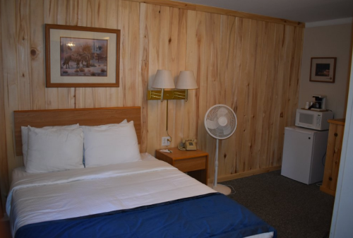 Cozy hotel room with a wooden wall, a bed, fan, microwave, and mini fridge.