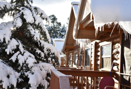 Snow-covered cabins line a wooden walkway, with a frosted tree nearby and icicles hanging from the roofs.