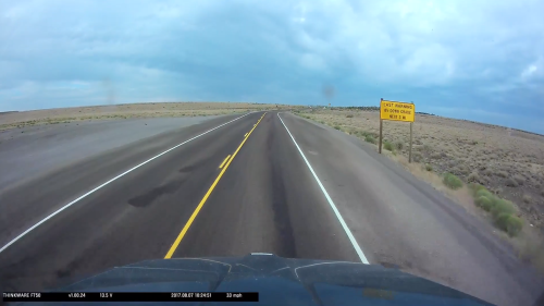 A wide, empty road stretches ahead with a sign warning of the last services for 65 miles in a desolate landscape.