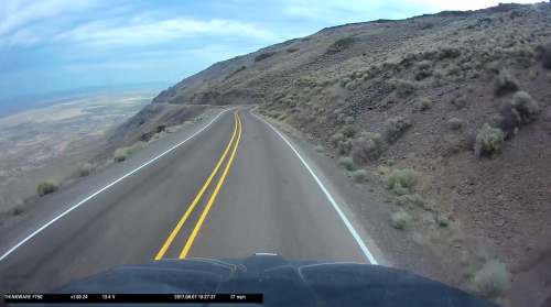 Winding road along a mountainous landscape under a cloudy sky, captured from a vehicle's perspective.