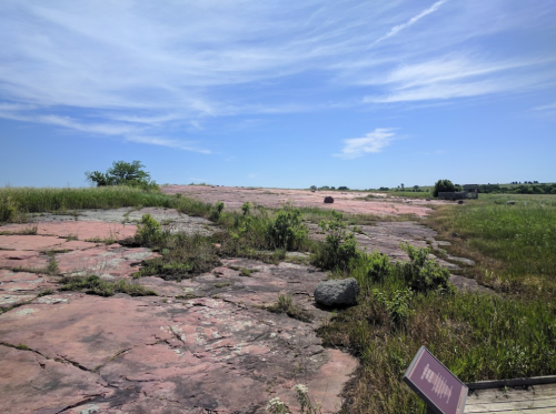 A rocky landscape with pink stone, sparse grass, and a clear blue sky in the background.