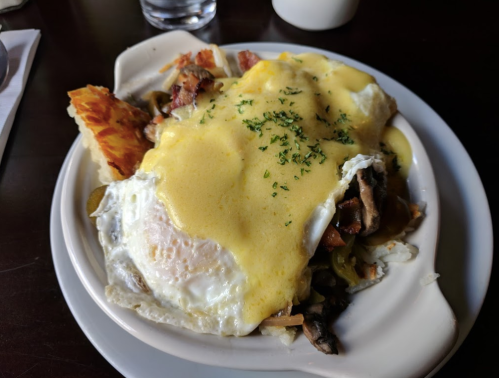 A plate of eggs topped with hollandaise sauce, mushrooms, and a side of crispy hash browns.