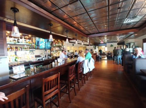 A spacious bar area in a restaurant with wooden seating, shelves of liquor, and patrons enjoying their time.