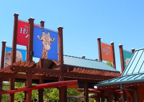 Entrance to the Utah Hogle Zoo, featuring colorful banners of animals against a clear blue sky.