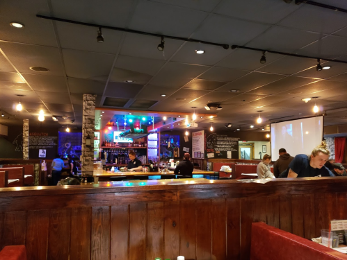 A lively restaurant interior with a bar, colorful lights, and patrons dining at booths.