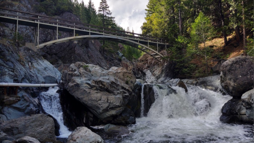A bridge arches over a rocky landscape with a flowing waterfall and lush greenery surrounding the scene.