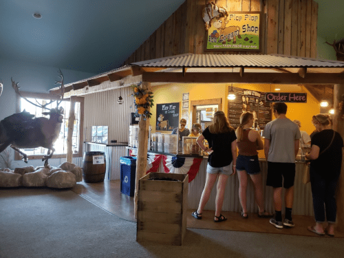 A rustic ice cream shop with customers ordering at the counter, featuring a mounted deer and decorative elements.
