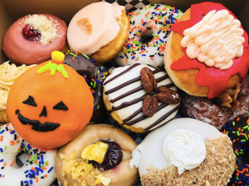 A colorful assortment of donuts, including a pumpkin-shaped one, topped with various icing and sprinkles.