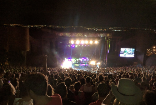 A large crowd enjoys a concert at Red Rocks Amphitheatre at night, with colorful lights illuminating the stage.