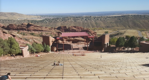 A wide view of Red Rocks Amphitheatre, showcasing the stage and surrounding natural landscape under a clear blue sky.