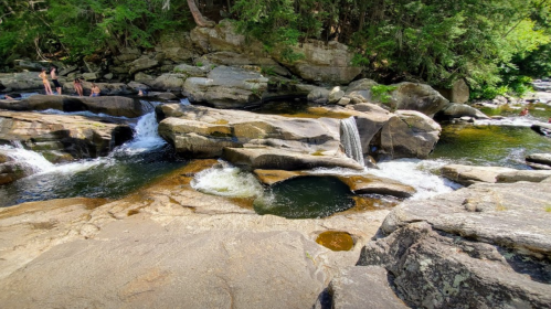 A serene river scene with smooth rocks, gentle waterfalls, and lush greenery surrounding the water.