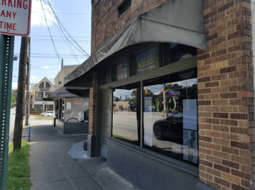 A corner storefront with a canopy, featuring large windows and a sign, set on a sunny street with power lines above.