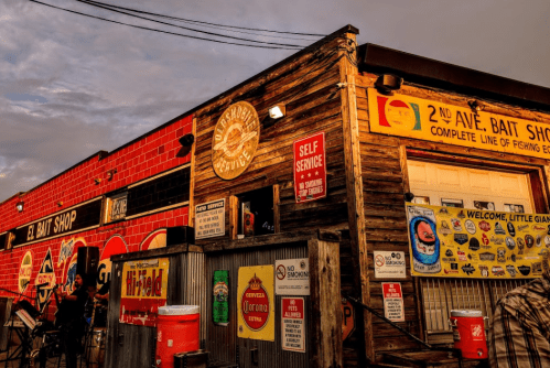 A rustic bait shop with colorful signage and a wooden exterior, set against a dramatic sky at sunset.