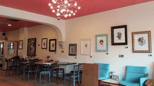 A cozy café interior with colorful walls, framed artwork, and modern furniture, featuring a unique chandelier.
