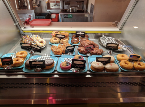 A display case filled with various donuts, including colorful sprinkles and vegan options, on blue trays.