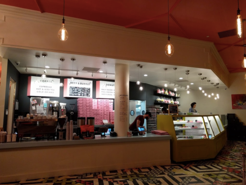 A cozy café interior with a coffee counter, menu boards, and a display case filled with pastries and donuts.