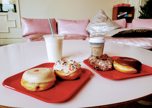 A table with two red plates holding donuts, a milkshake, and a coffee cup in a cozy cafe setting.