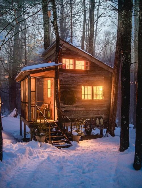 A cozy wooden cabin in a snowy forest, warmly lit from within, surrounded by trees and a serene winter landscape.