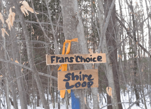 Wooden signs on a tree indicate "Fran's Choice" and "Shire Loop" trails in a snowy forest.