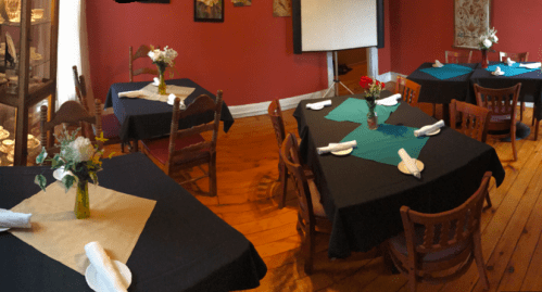 A cozy dining room with several tables set with black and teal tablecloths, flowers, and napkins, against a red wall.