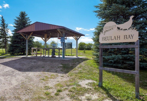 A wooden shelter with a sign reading "Beulah Bay" surrounded by trees and open sky.