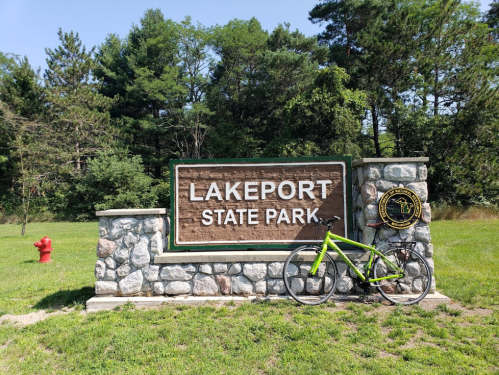 Sign for Lakeport State Park with a green bicycle leaning against a stone structure in a grassy area.