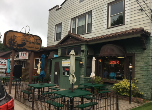 A cozy diner with green and wooden exterior, outdoor seating, and a sign reading "Diner" in a quaint setting.