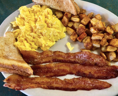 A plate of scrambled eggs, crispy bacon strips, golden-brown potatoes, and toasted bread.