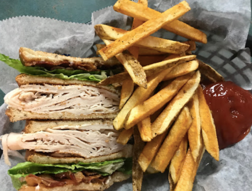 A sandwich with turkey, lettuce, and bacon, served with crispy fries and ketchup on the side.