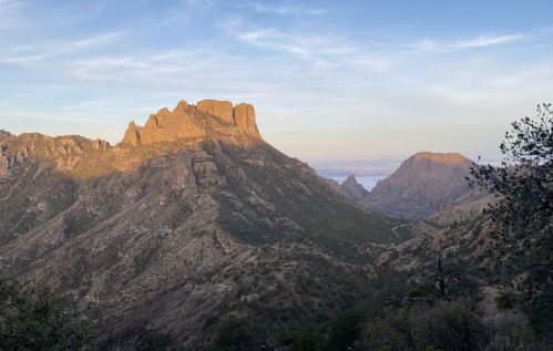 A rugged mountain landscape at sunset, with golden light illuminating the peaks and valleys under a clear sky.