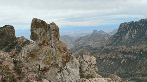 A rocky landscape with rugged mountains and a cloudy sky in the background, showcasing natural formations and valleys.