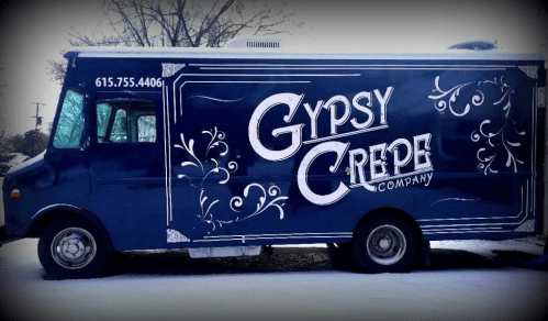 A blue food truck with "Gypsy Crepe Company" written in decorative white letters, parked on a snowy street.