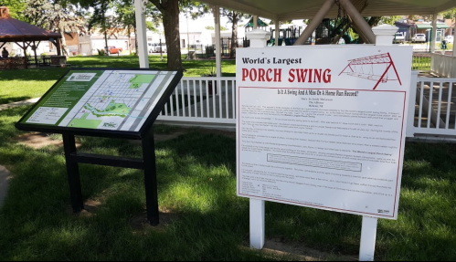 Signage for the World's Largest Porch Swing in a park, with a map and informational display nearby.