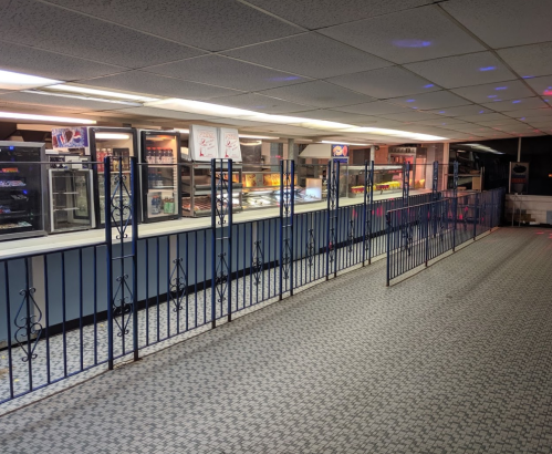 Interior of a diner with a counter, display cases, and a patterned floor, featuring a blue fence-like barrier.