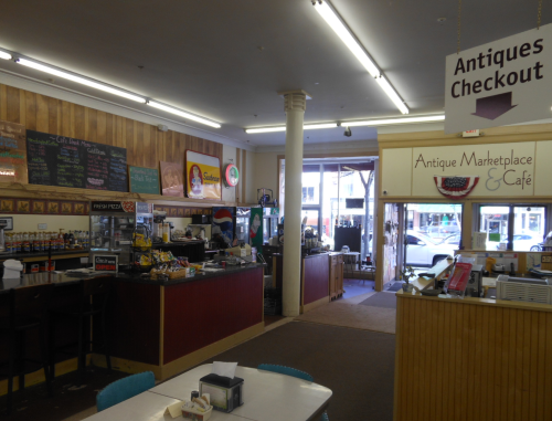 Interior of an antique marketplace and café, featuring a checkout area, shelves of items, and a cozy dining space.