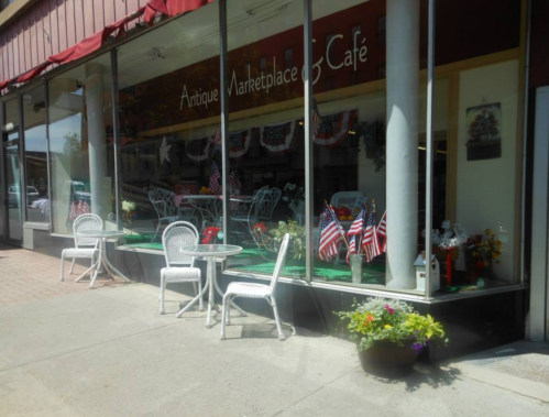 A quaint café with outdoor seating, decorated with flowers and small American flags, in a charming marketplace setting.