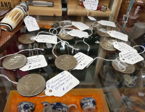 A display of coins with price tags, arranged on a glass surface, featuring various denominations and details.