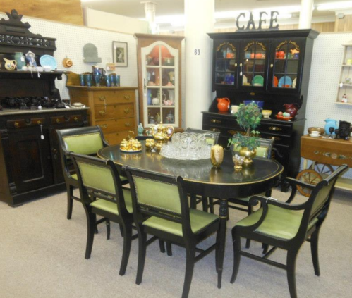 A vintage dining room setup featuring a black table, green chairs, and various decorative items on display.