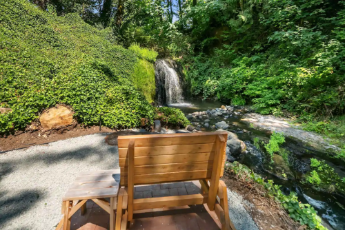 A wooden bench overlooks a serene waterfall surrounded by lush greenery and a rocky stream.