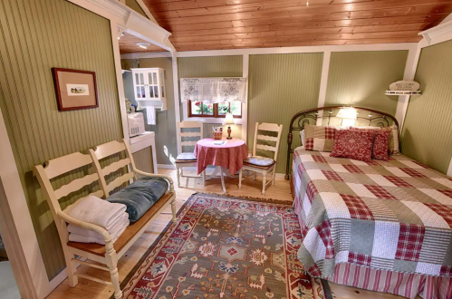 Cozy room with a bed, dining table, and rustic decor, featuring green walls and a patterned rug.