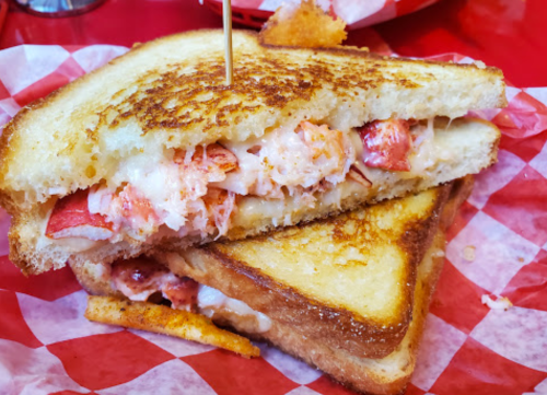 A close-up of a grilled cheese sandwich filled with lobster, served on red and white checkered paper.