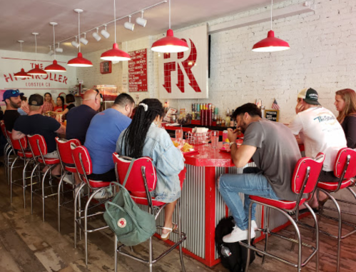 A lively restaurant interior with patrons seated at a red bar, enjoying food and drinks in a casual atmosphere.