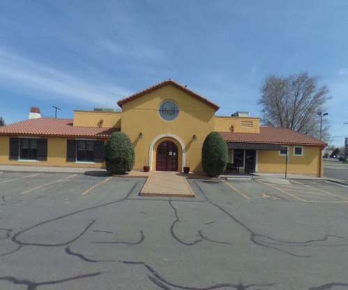 A yellow building with a red tile roof, featuring a central entrance and two large shrubs on either side.