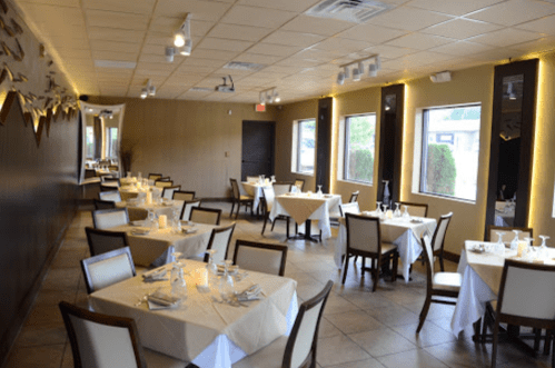 A spacious restaurant interior with neatly set tables, soft lighting, and large windows.