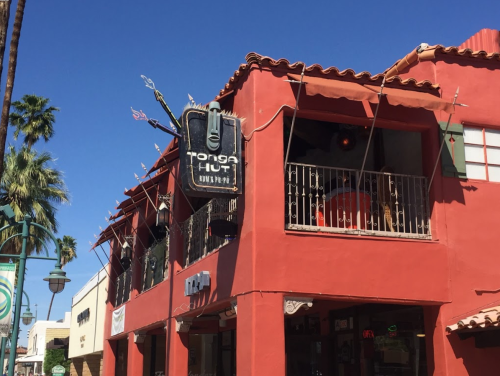 A vibrant red building with a sign for "Tonga Hut," featuring tropical decor and a clear blue sky above.